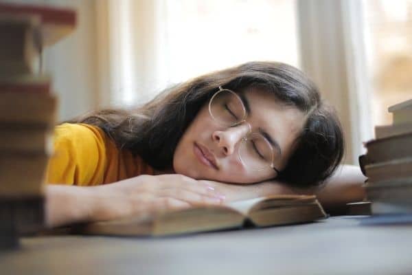 woman asleep on an open book surrounded by piles of books