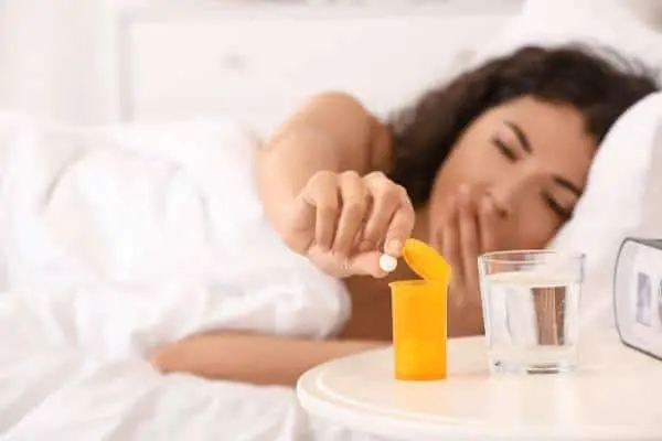 woman in bed reaching for a sleeping pill and yawning 