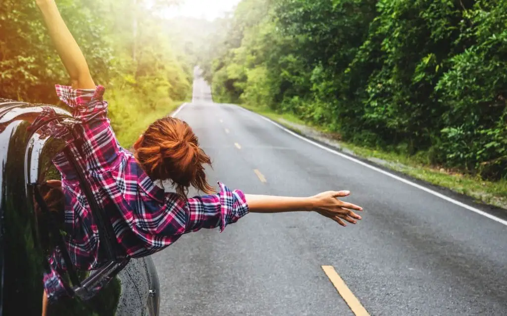 a woman hanging out the side of a car driving in a beautiful location