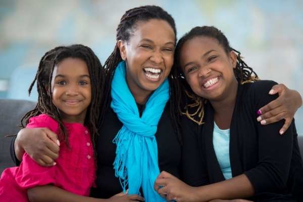 A mom smiling and hugging her two daughters