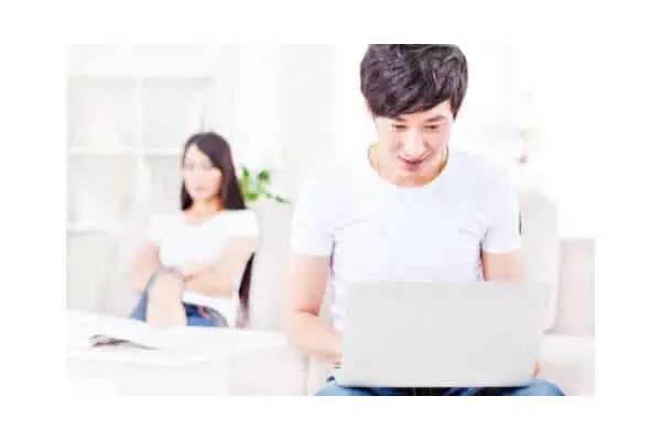 man looking at computer screen with interest as woman behind him looks upset at being ignored