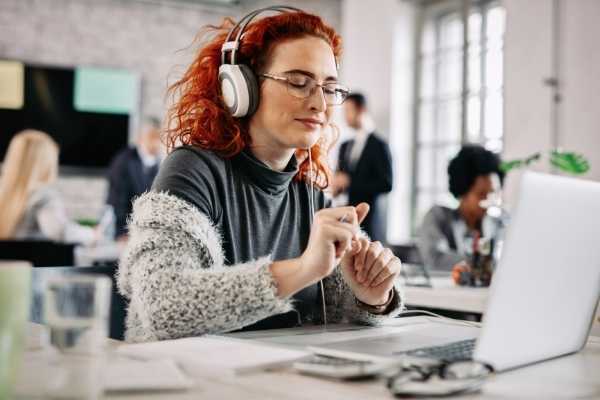 relaxed looking woman wearing headphones at a work desk  in open office