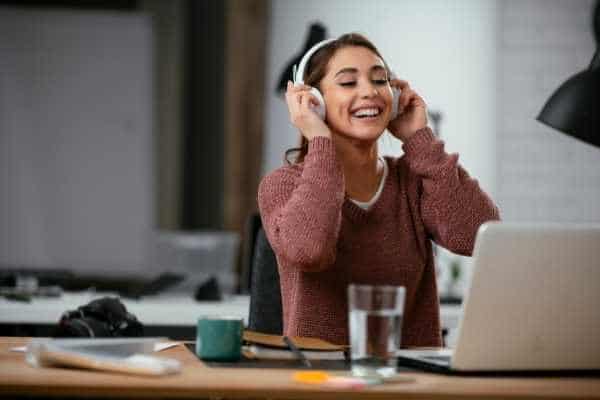 smiling woman wearing headphones at a desk with a laptop