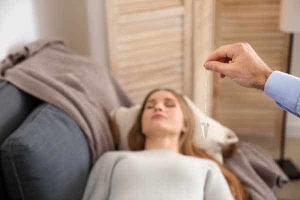 woman lying on a couch with a person holding a hypnotizing pendant in front of her