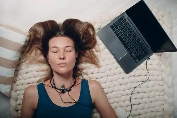 woman looking relaxed lying down listening to headphones attached to a laptop