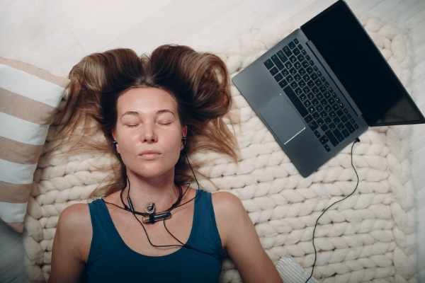 woman lying down listening to headphones attached to a laptop