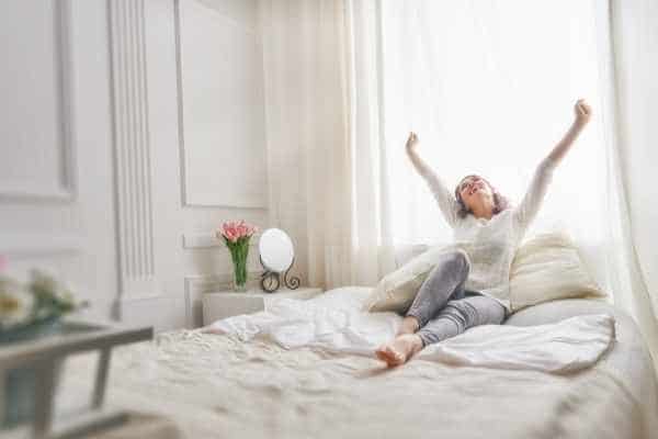 woman waking up in bed stretching her arms looking refreshed