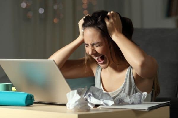 a very stressed out woman in front of a laptop holding her head and screaming