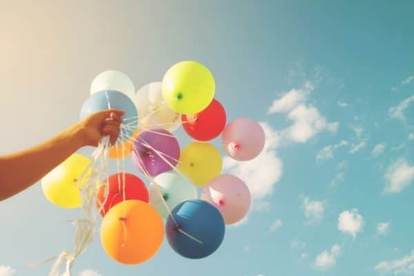 a hand holding several balloons in front of a cloudy sky