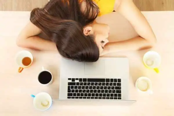 woman asleep in front of an open laptop with several empty cups of coffee