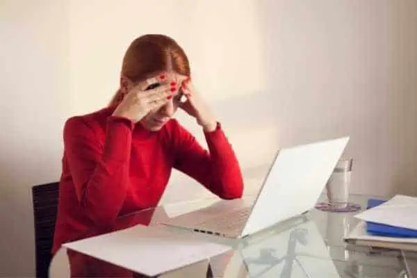 woman sitting at a desk in front of a laptop looking stressed and holding her head in her hands