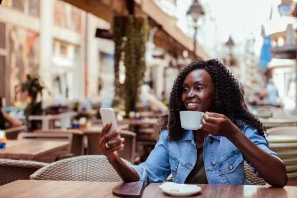 woman looking a her phone at an outdoor cafe with a cup of coffee