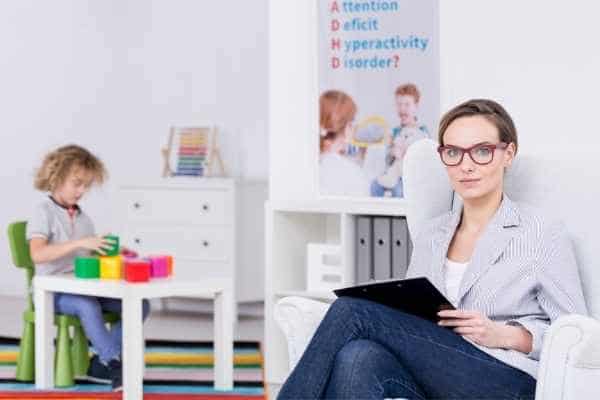 A researcher in a room with a child with a poster saying Attention Deficit Hyperactivity Disorder on the wall