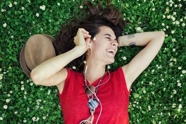 a woman lying on the grass enjoying music she is hearing through ear buds