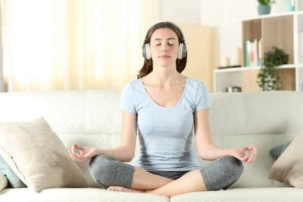 woman meditating while sitting on a couch with headphones on