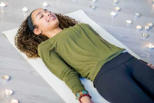 young woman lying on a yoga mat surrounded by candles