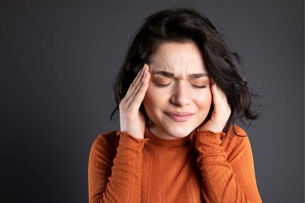 woman with headache holding her temples and wincing