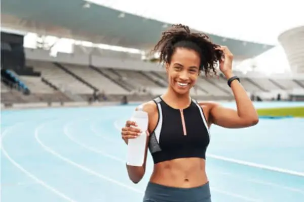 woman on a track field smiling and holding a water bottle